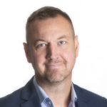 Portrætfoto af Björn Nilsson i mørkeblå jakke og lyseblå skjorte mod hvid baggrund.
