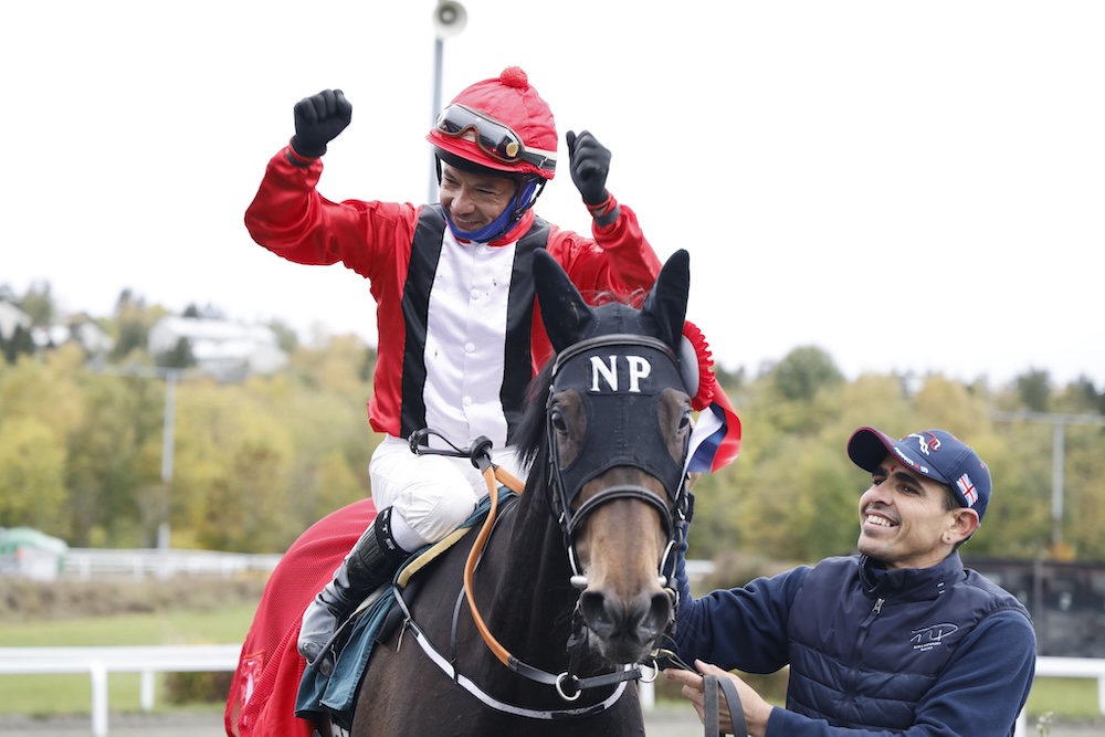 Carlos Lopez løfter knytnæven i rød dragt på Lady Irene efter sejren i Norsk Oaks, mens en staldmedarbejder tager imod på Øvrevoll.
